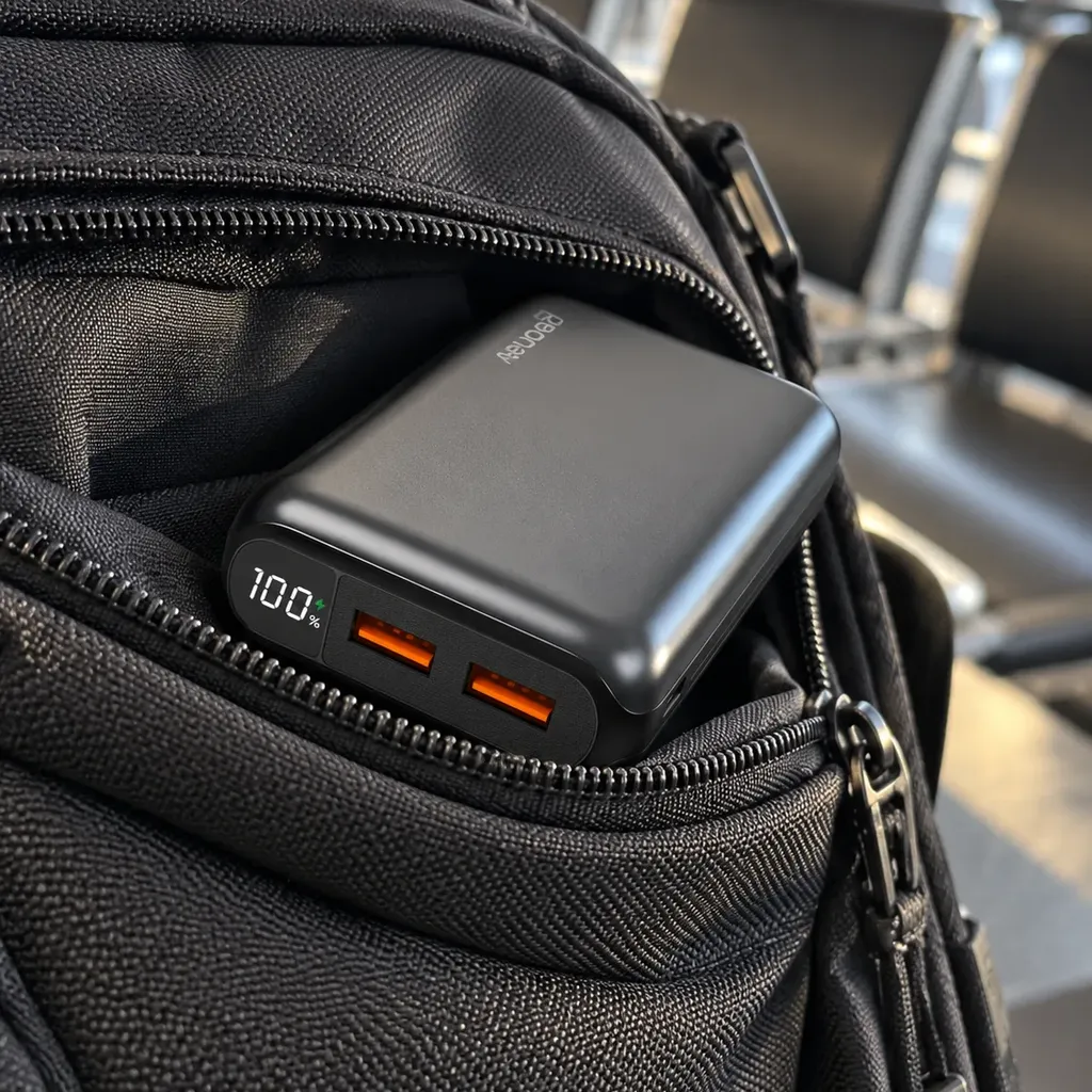 Carregador GeoNav de 20.000 mAh saindo do bolso da mochila, com a tela em 100% e as duas portas USB laranja à mostra